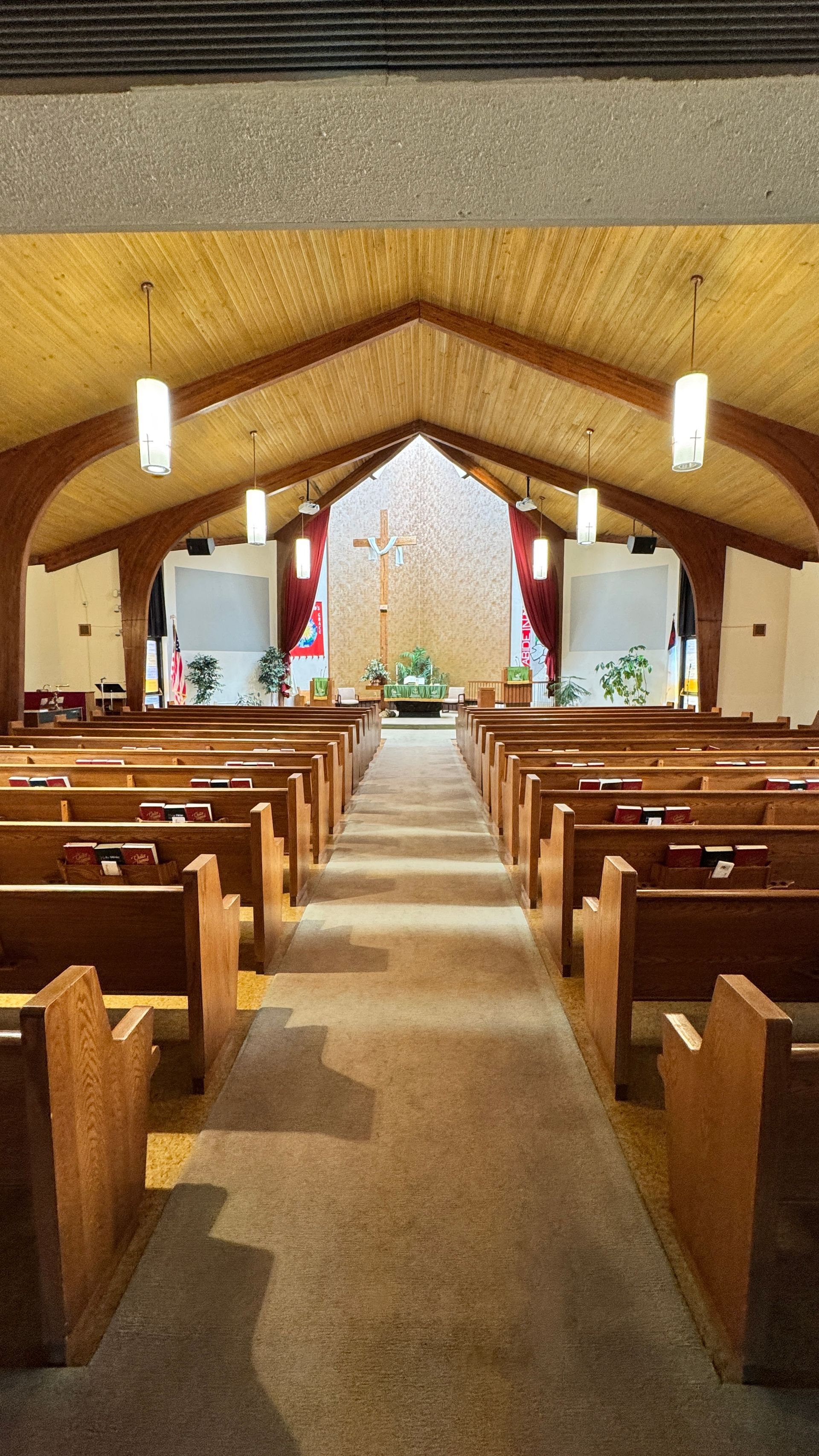 The inside of a church with rows of wooden benches and a cross on the altar.