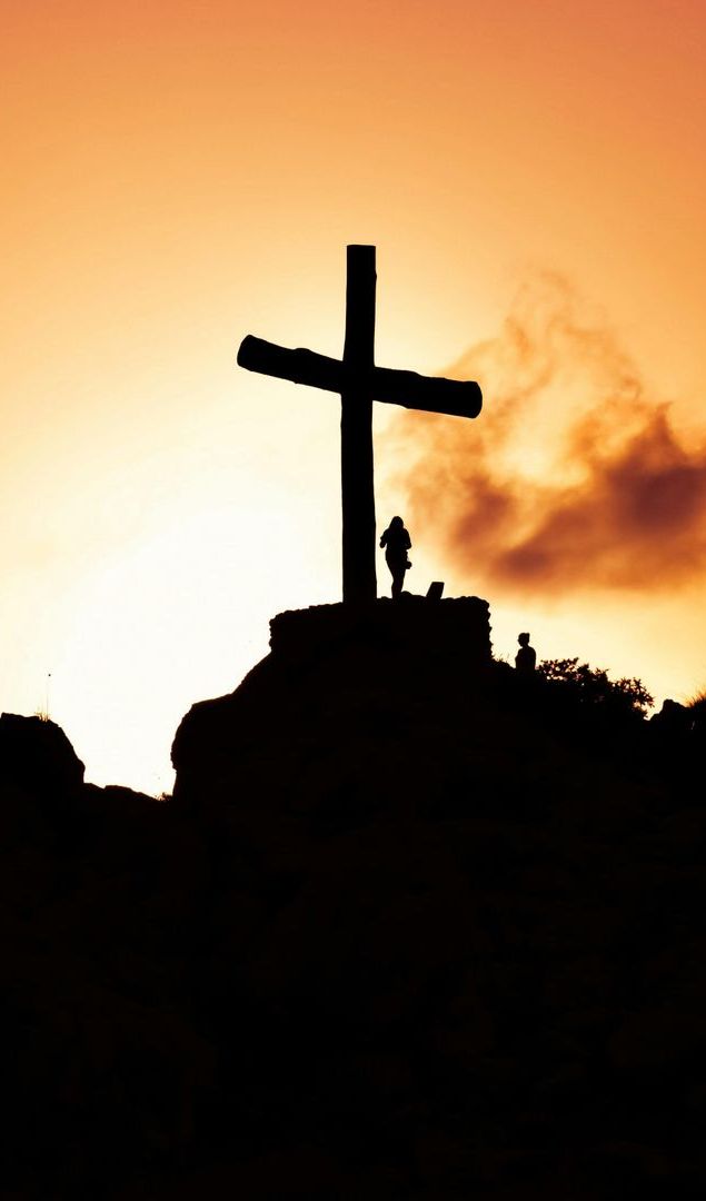 A silhouette of a cross on top of a hill at sunset