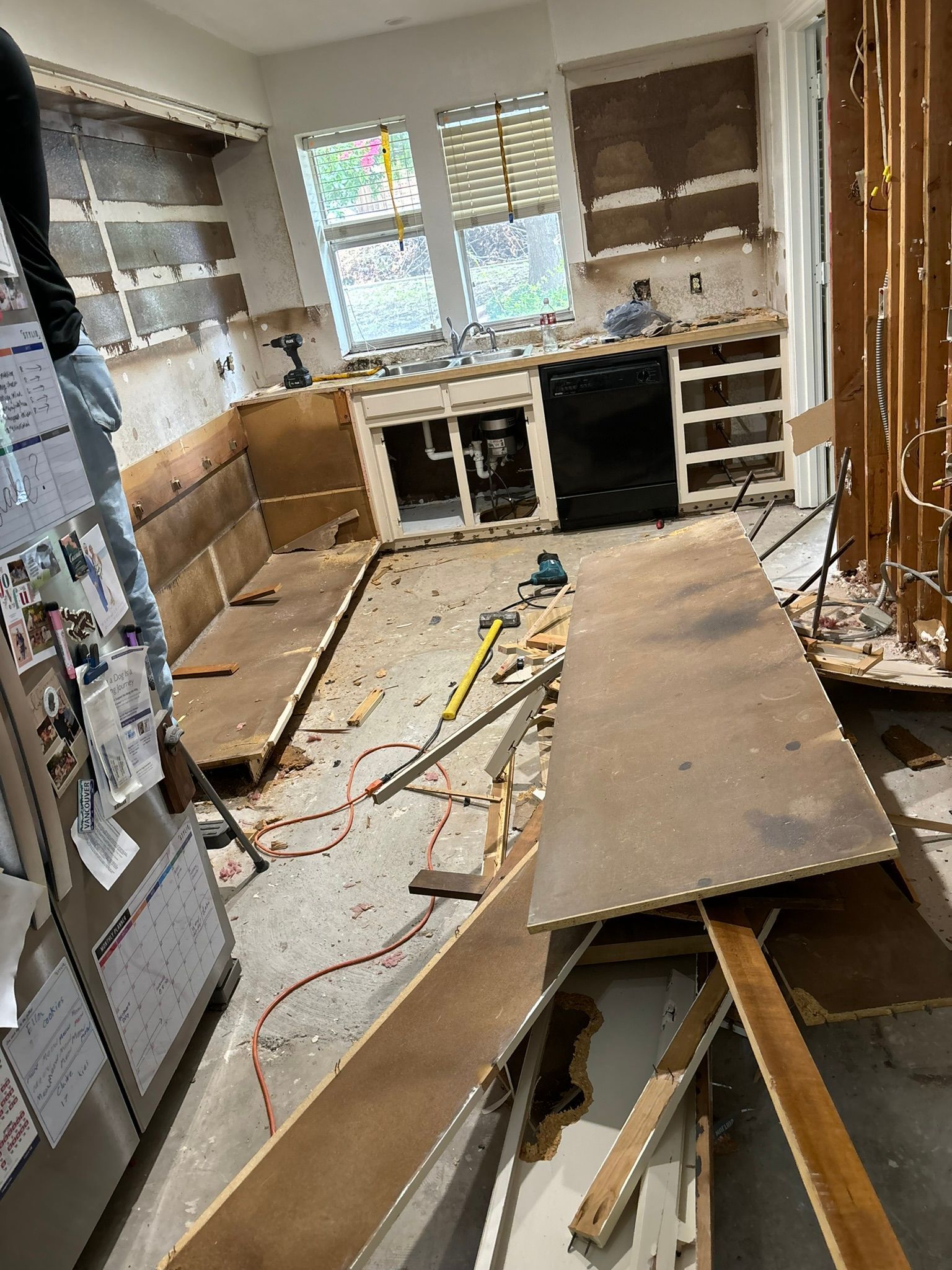 A kitchen under renovation with exposed wall studs, missing countertops, cabinet frames, and debris on the floor.