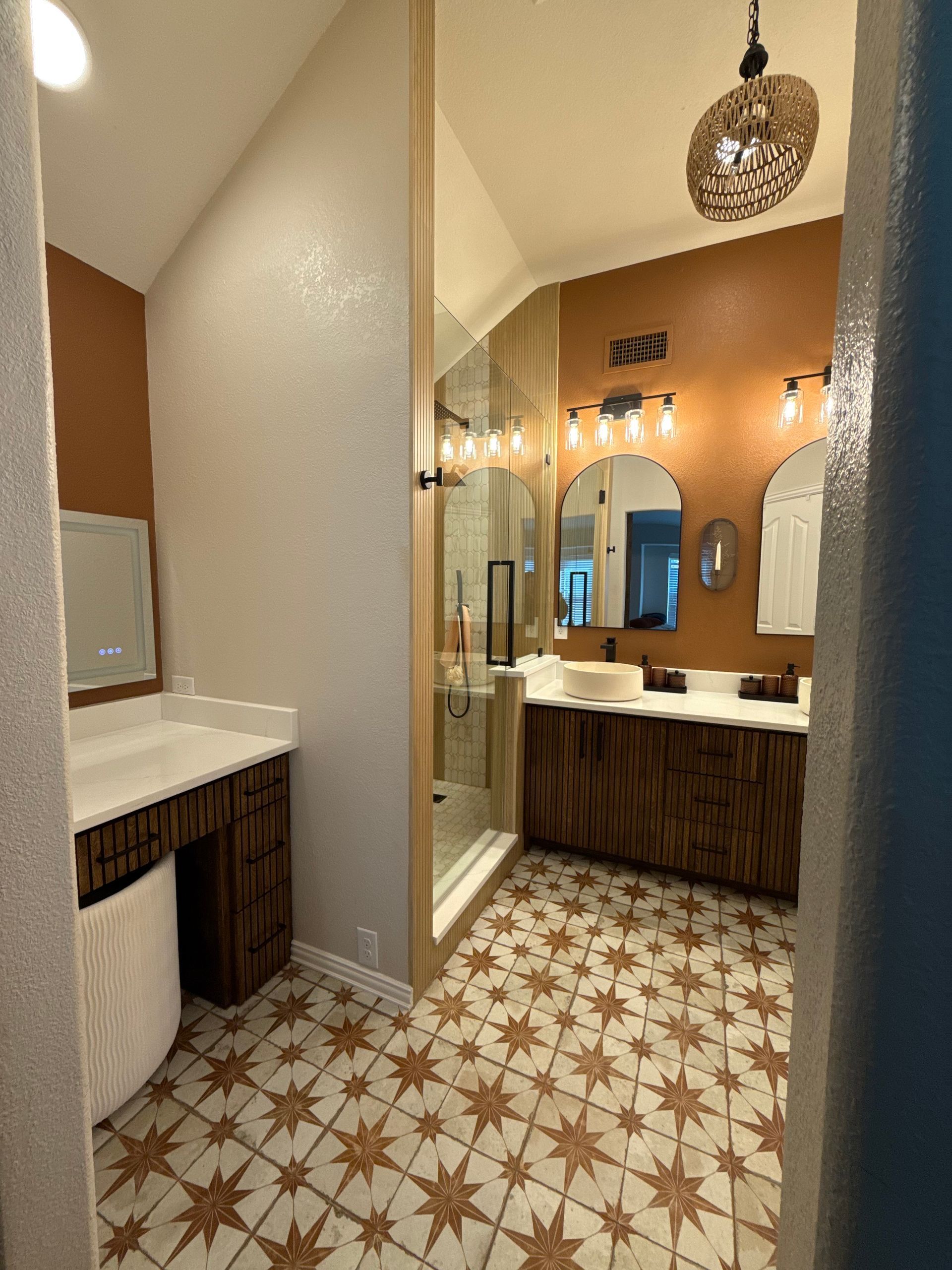 Bathroom with star-patterned tile floor, brown and white walls, wooden vanities, glass shower, and decorative light fixtures.