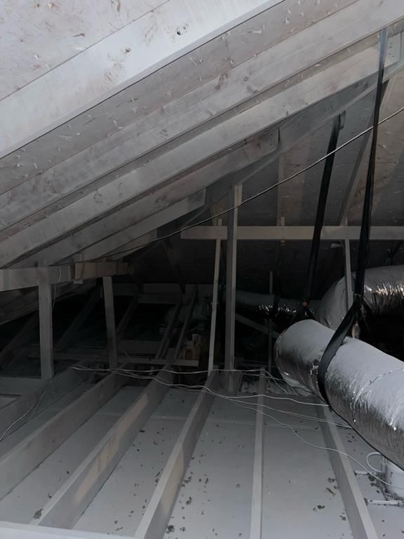 An unfinished attic interior with wooden ceiling rafters, exposed floor joists, and hanging HVAC ducts.