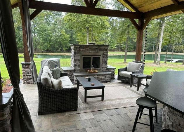 Covered patio with wicker chairs and a stone fireplace overlooking a green yard