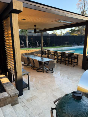 Covered patio with dining table, chairs, and grill beside a backyard swimming pool.