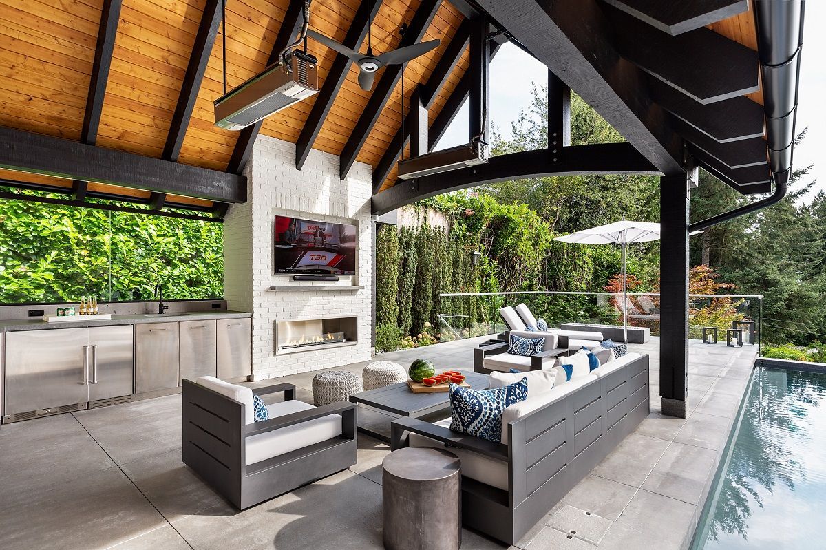 Modern outdoor patio with gray seating, kitchen, and pool under a wood-beamed roof
