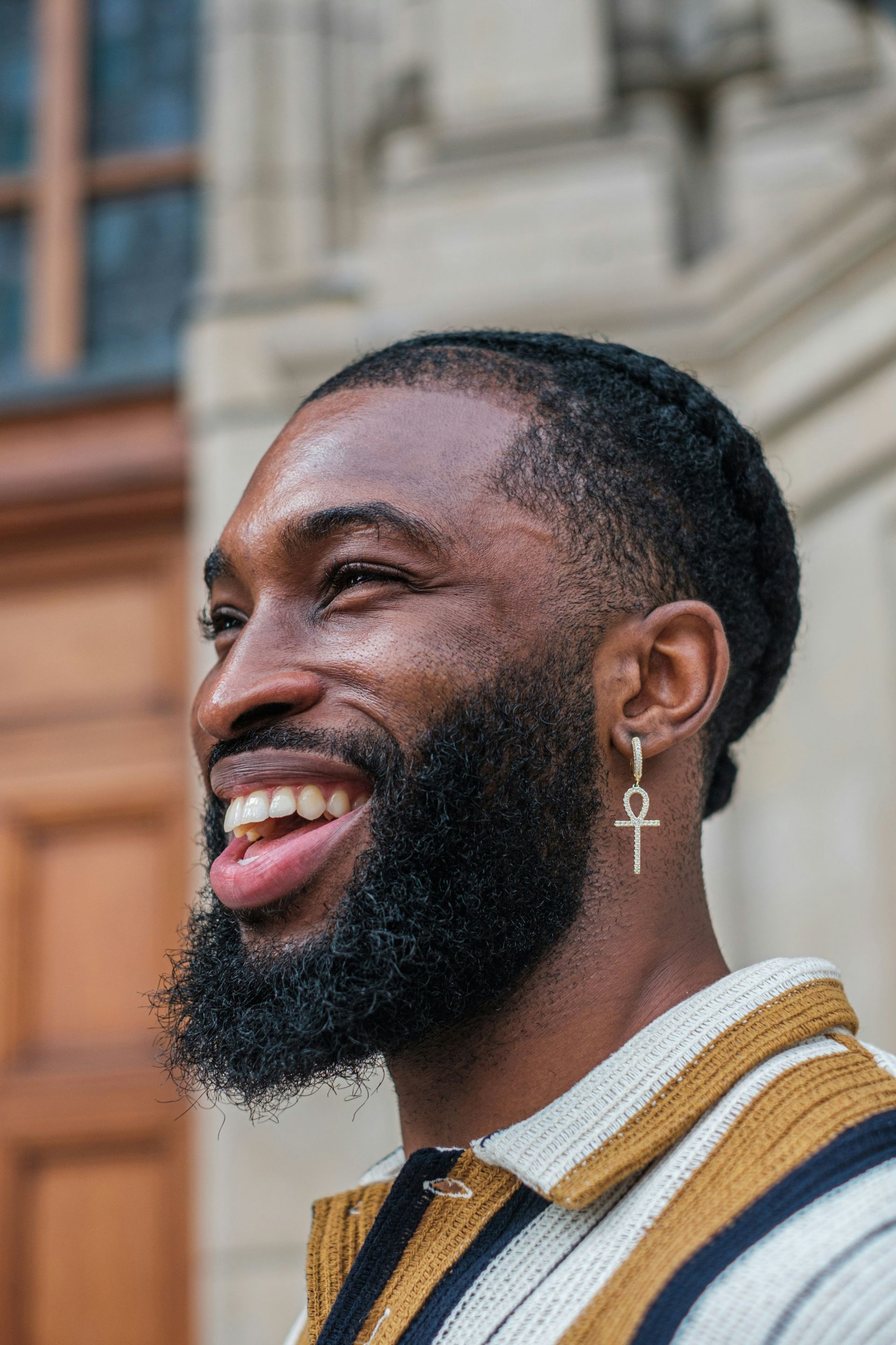 Man with beard smiling, wearing ankh earring, outdoors.