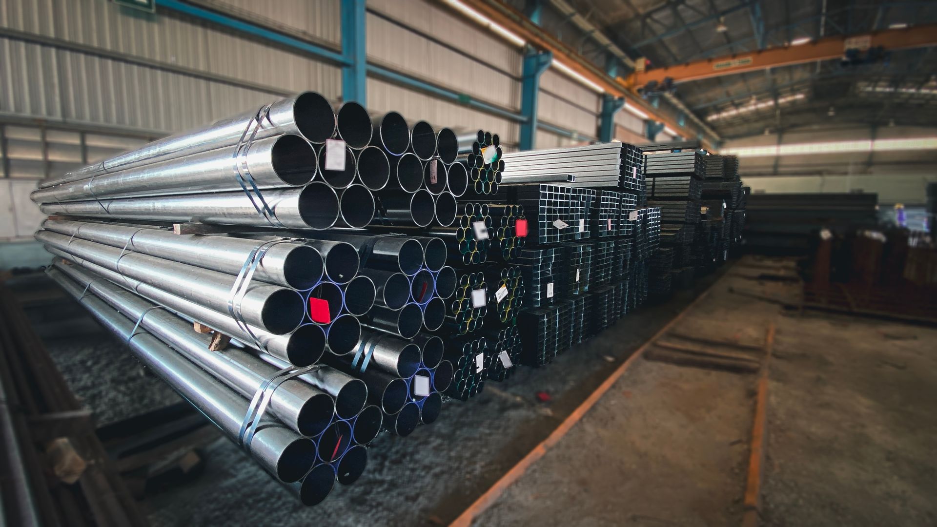 Piles of steel pipes stacked in an industrial warehouse setting with overhead crane. Piles of steel pipes stacked in an industrial warehouse setting with overhead crane.