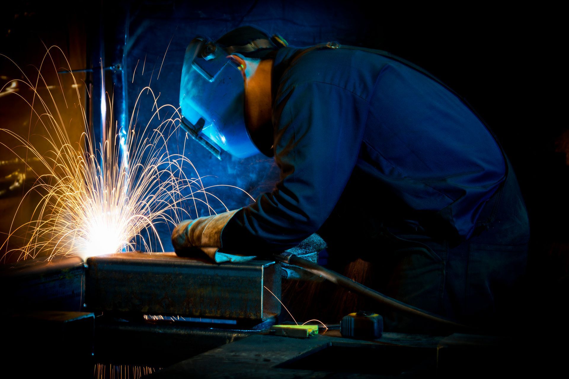 Welder engrossed in structural steel fabrication, sparks flying as they work.
