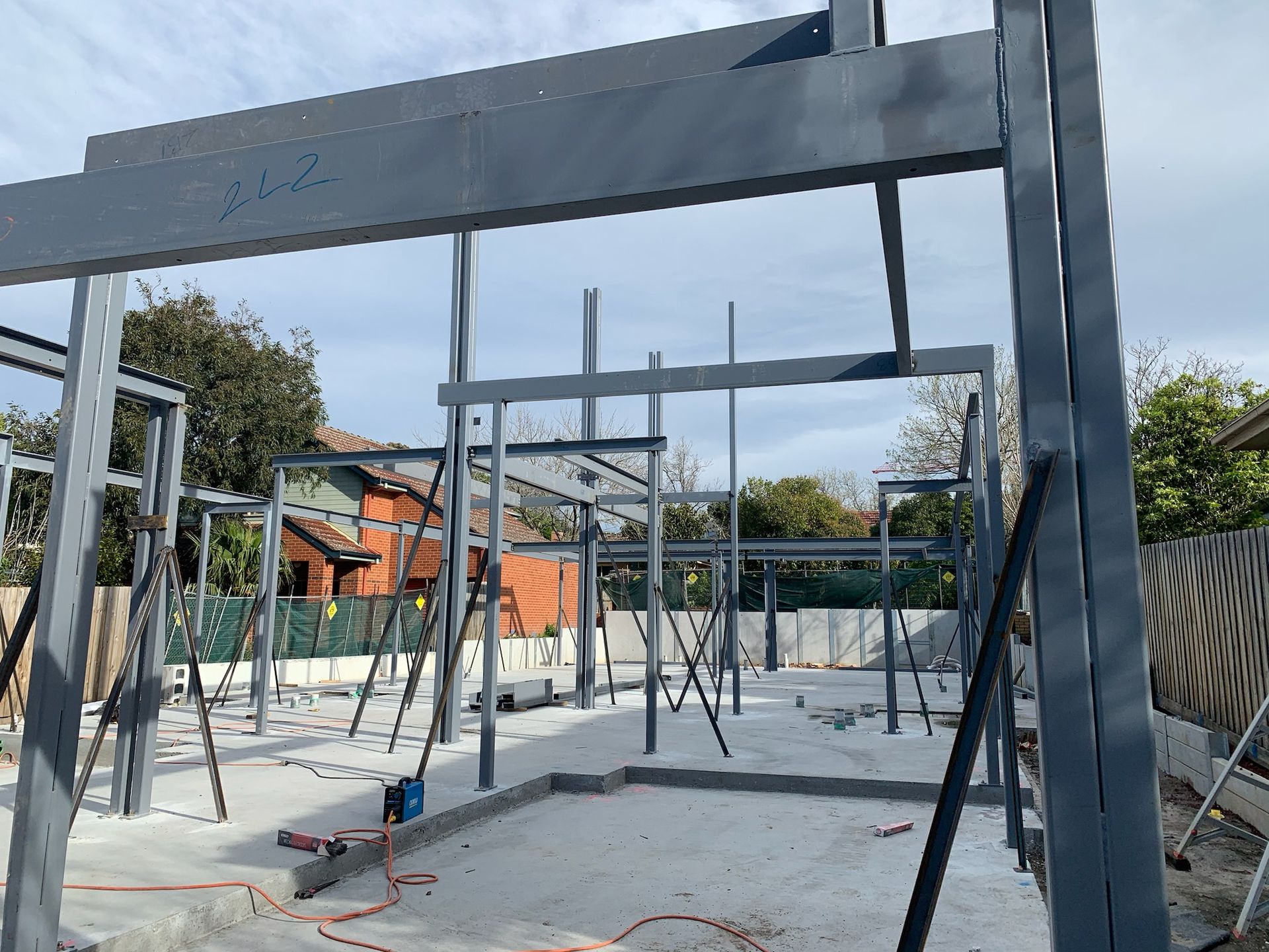 Steel frame of a building under construction, grey beams, concrete foundation, outdoor setting in Melbourne.