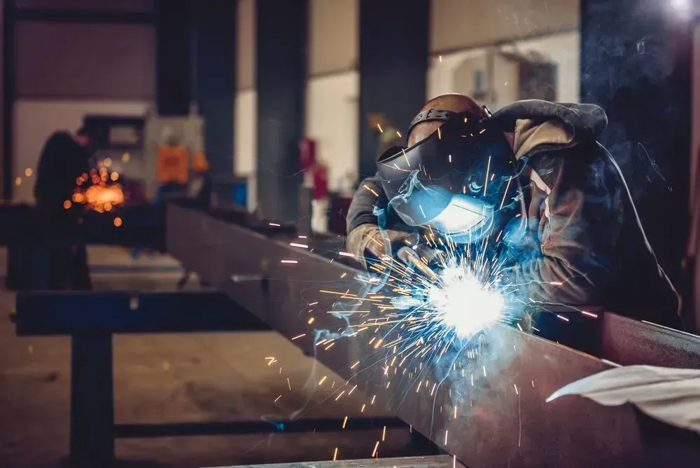 A man is welding a metal pipe in a factory.