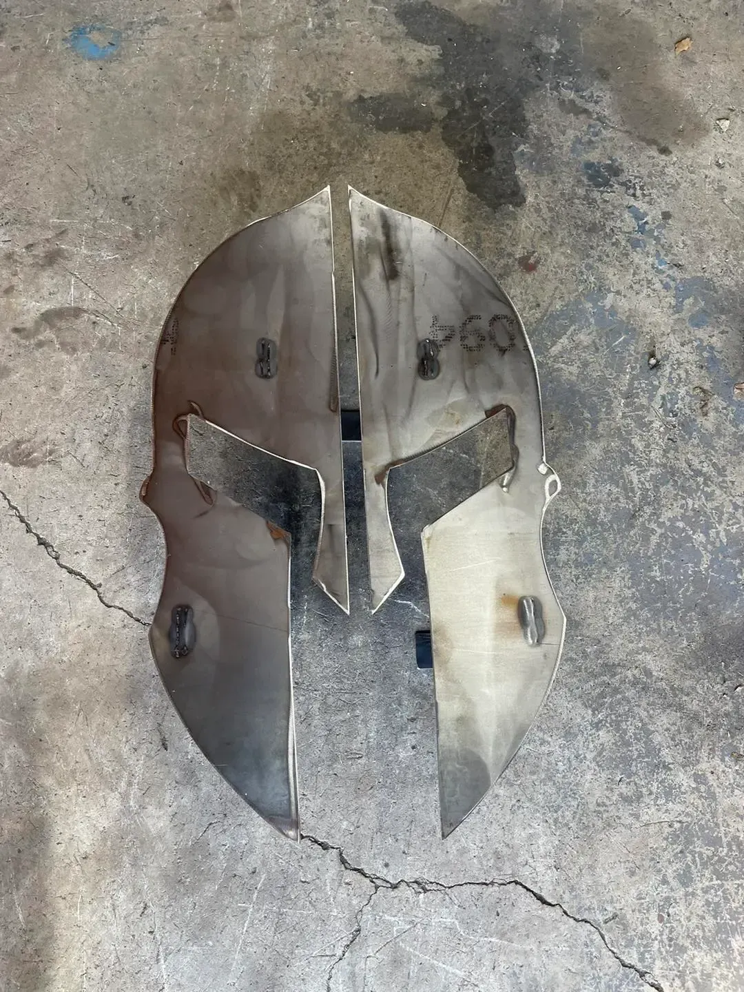A metal spartan helmet is sitting on a concrete surface.