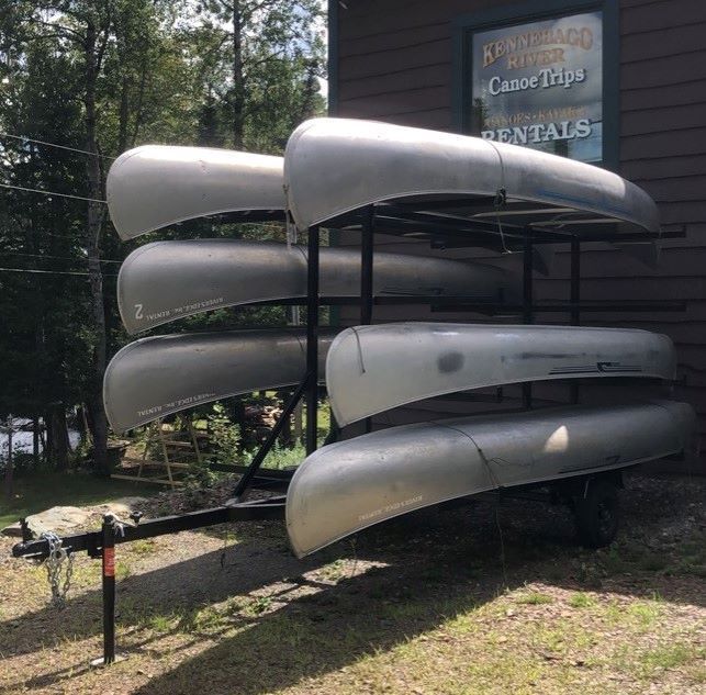 A trailer filled with canoes is parked in front of a building.