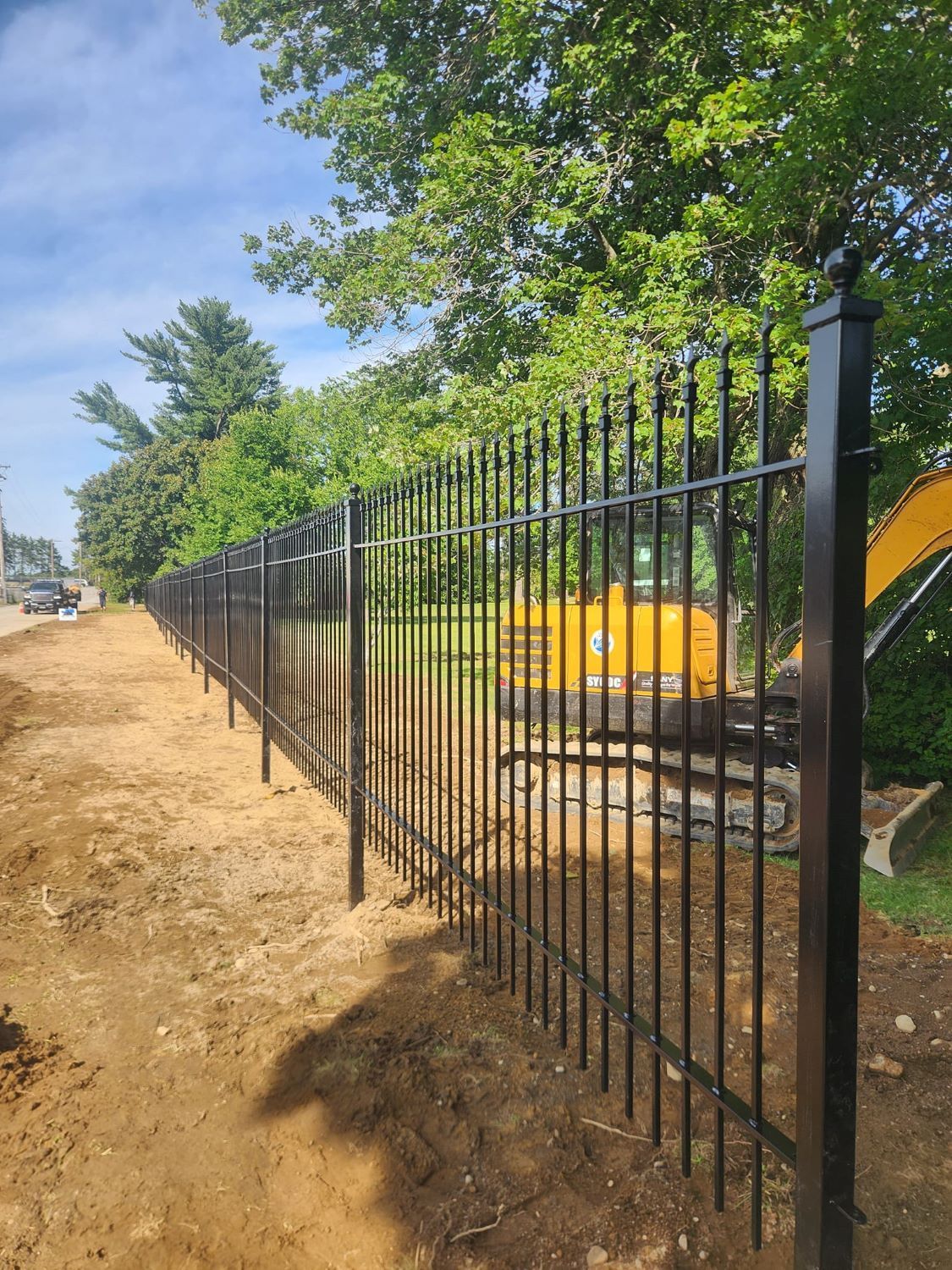 A black metal fence is being built next to a dirt road.