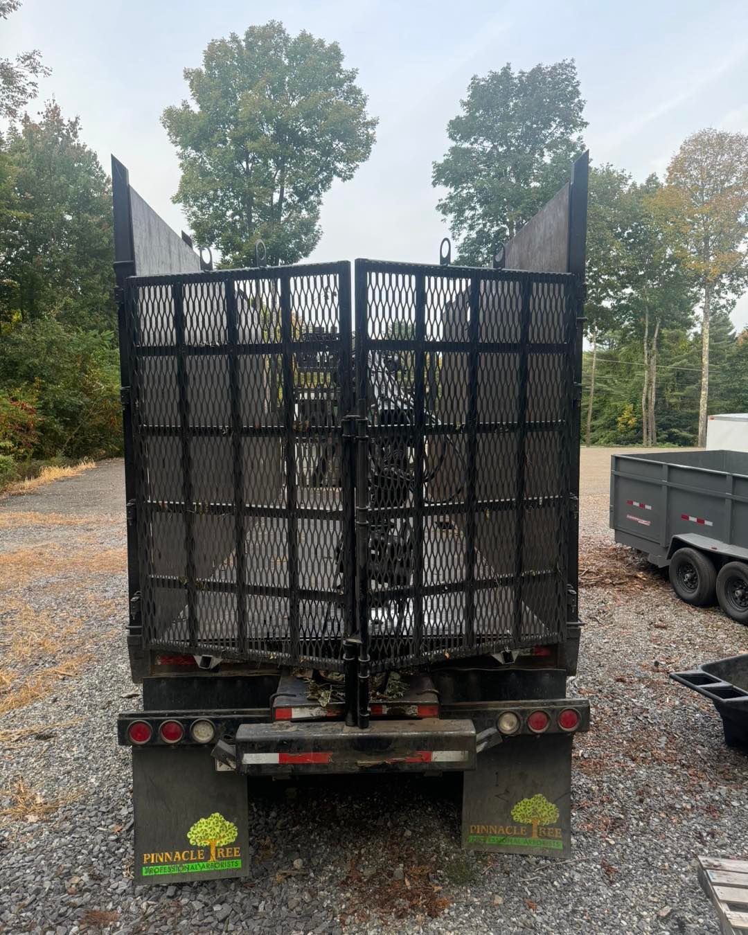 A dump truck is parked in a gravel lot with trees in the background.