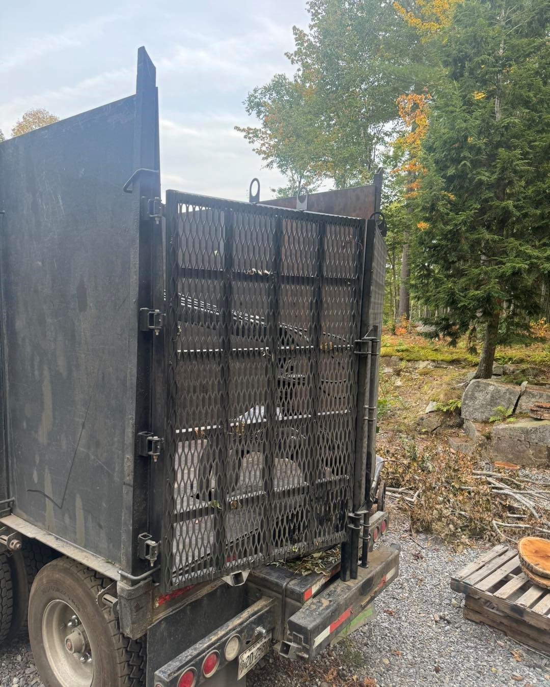 A dump truck with a cage on the back is parked in a gravel lot.