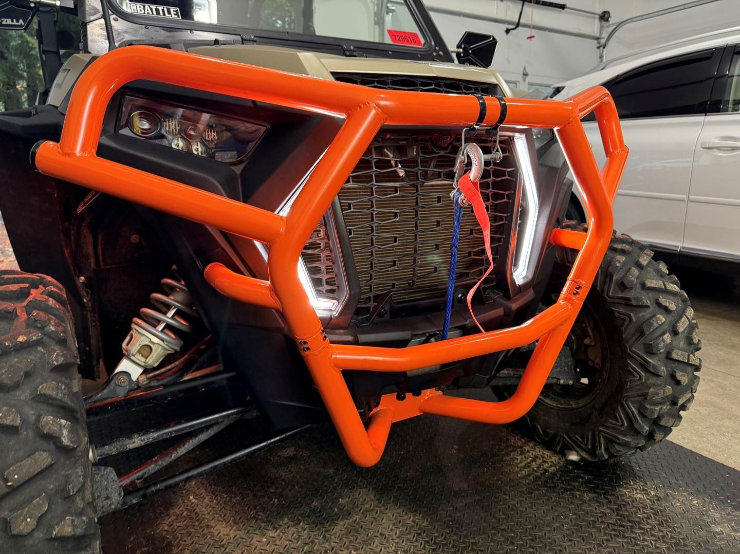 A polaris rzr 1000 with an orange bumper is parked in a garage.