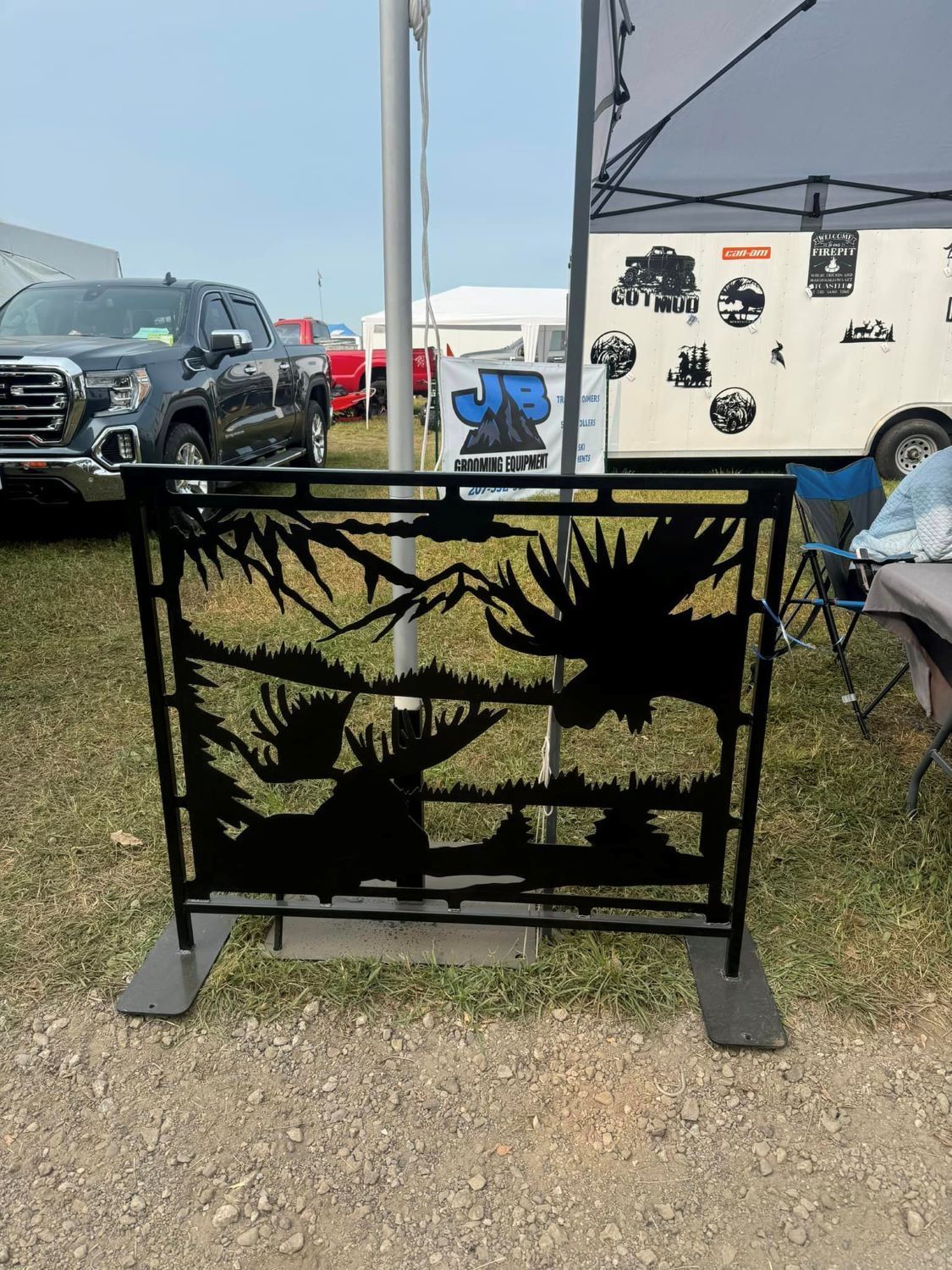 A metal fence with a moose on it is sitting in the grass.
