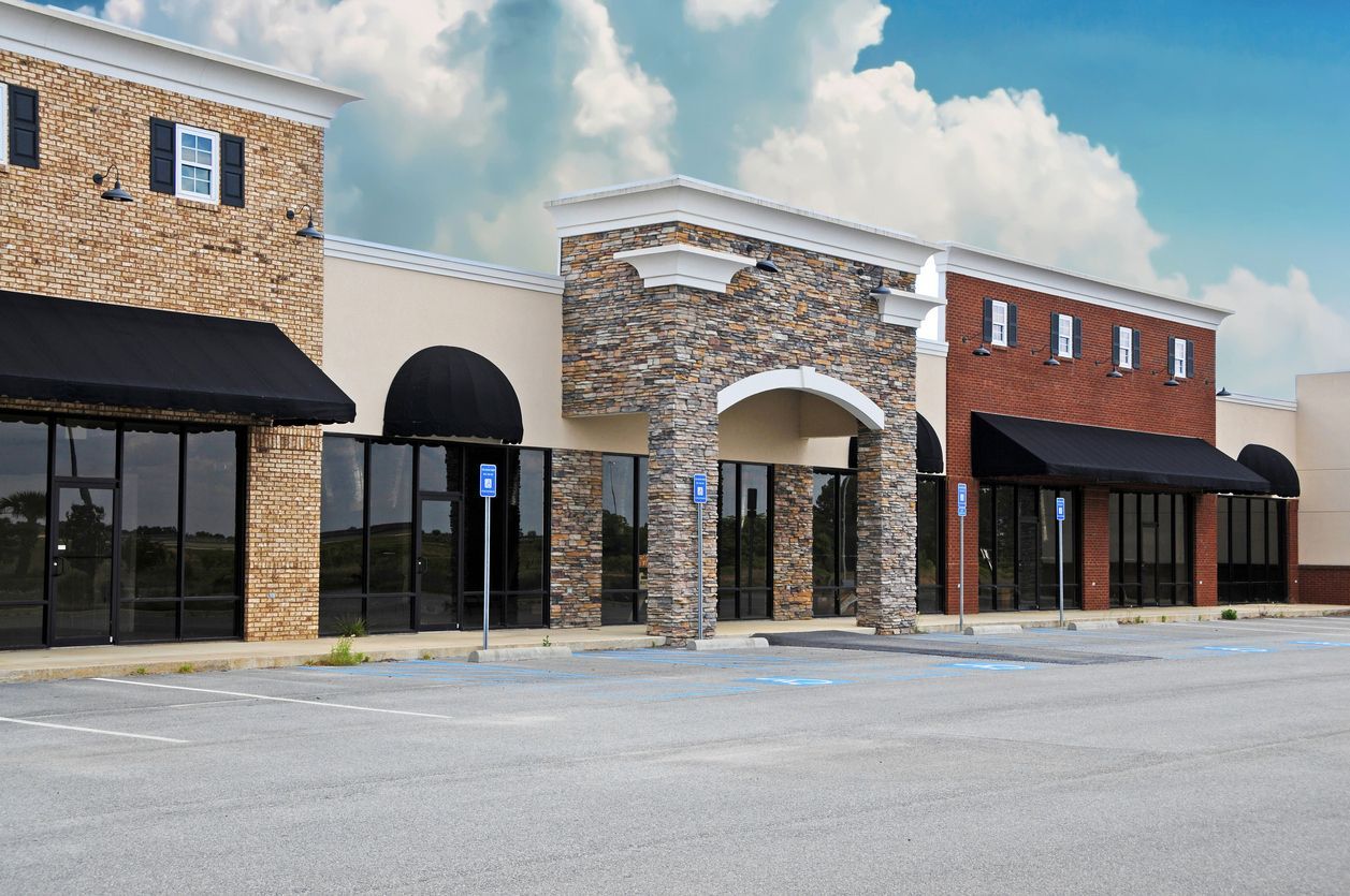 Empty storefronts in a strip mall with stone and brick facades under a cloudy sky