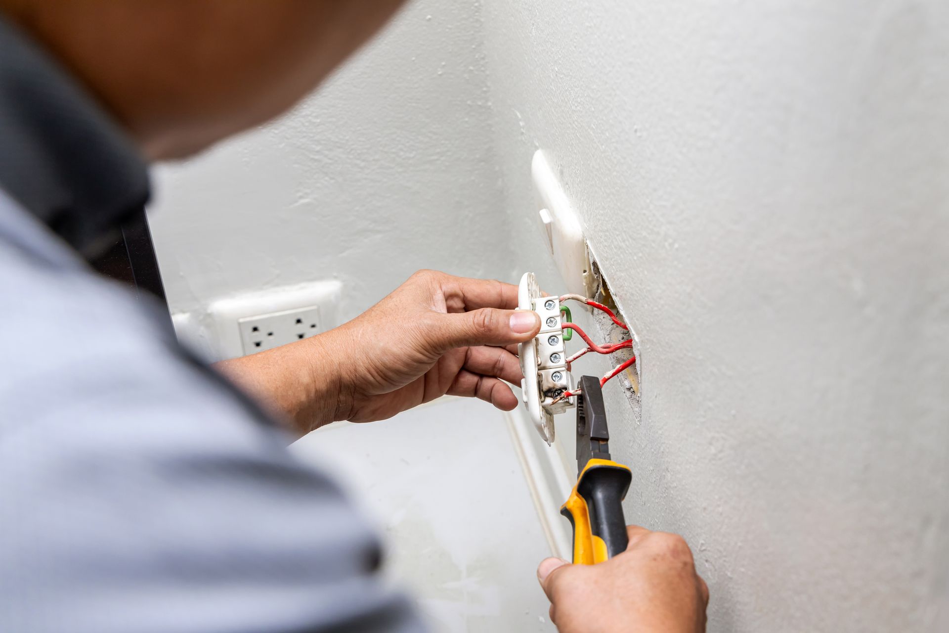 Electrician wiring an outlet with pliers and screwdriver on a wall panel