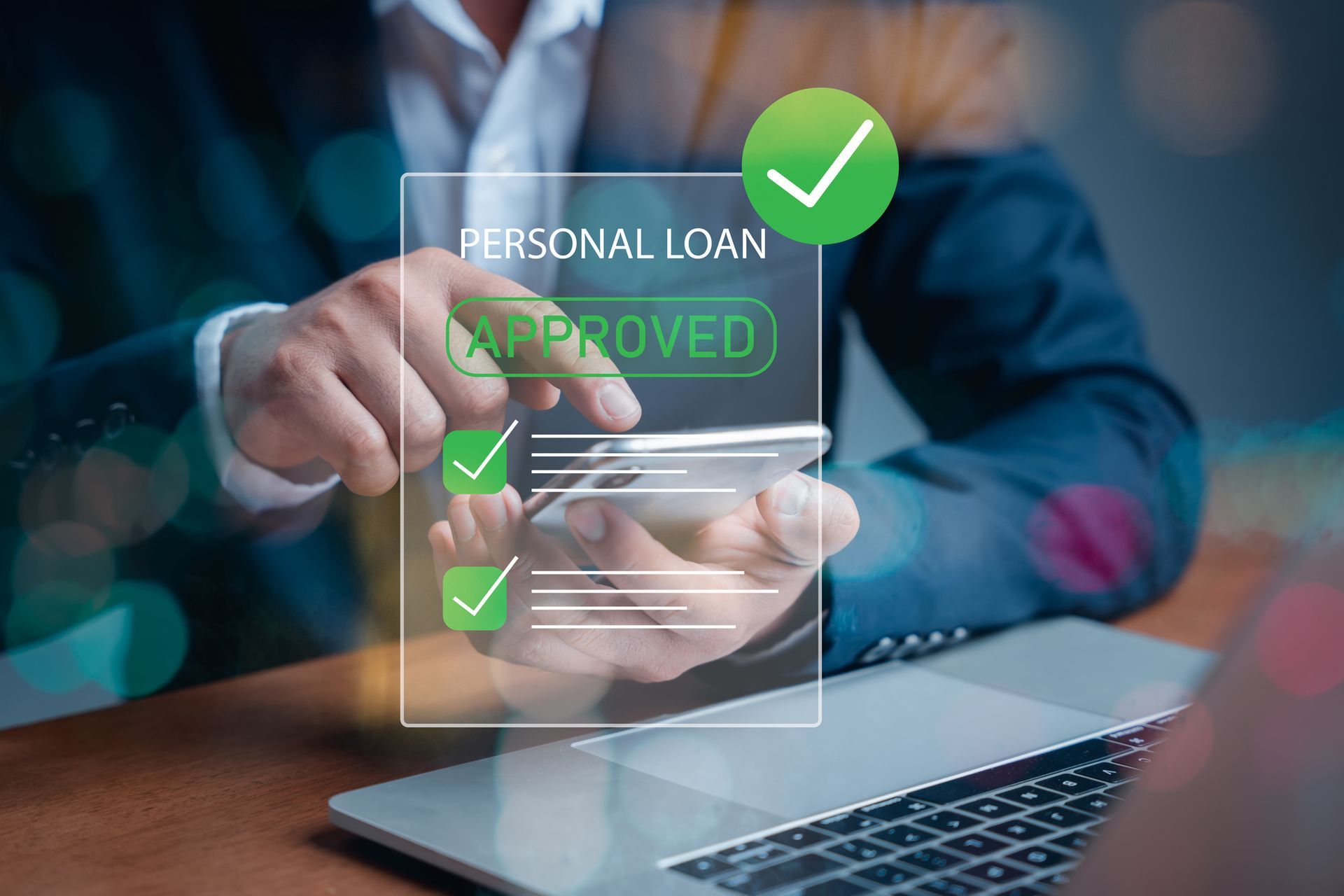 Hand holding phone showing “Personal Loan Approved” with green check marks beside a laptop