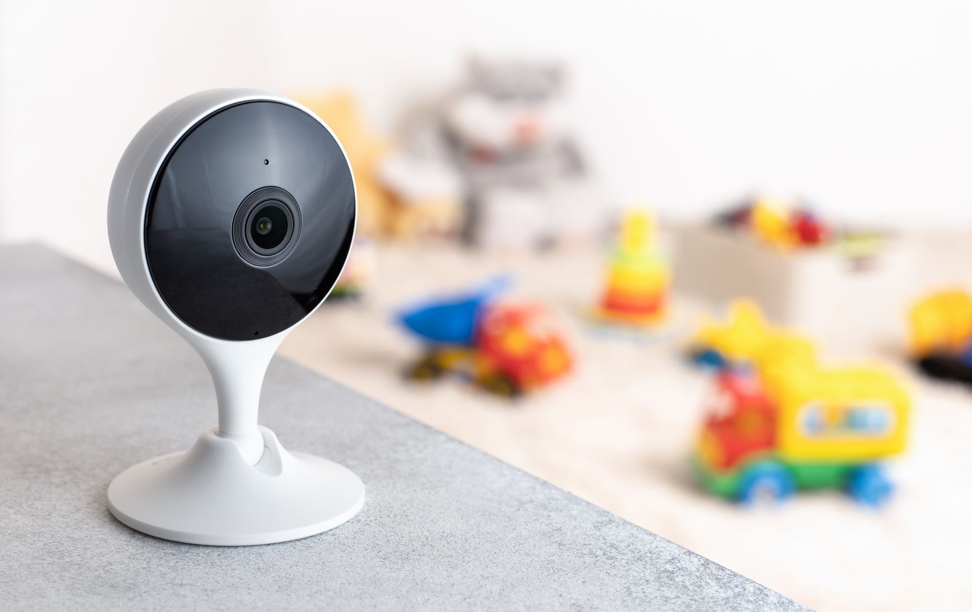 Black-and-white security camera on a table, with blurred colorful toys in the background