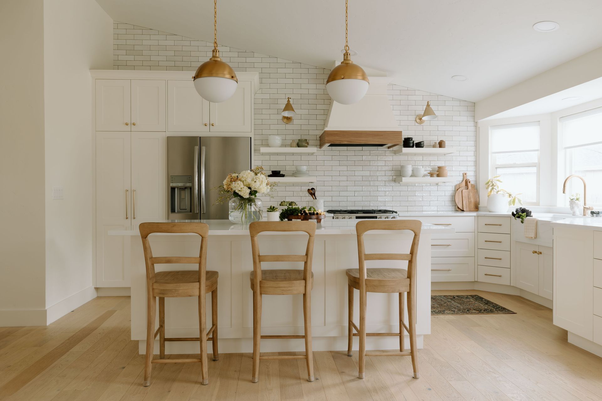 Bright white kitchen with wood island, bar stools, pendant lights, and large windows