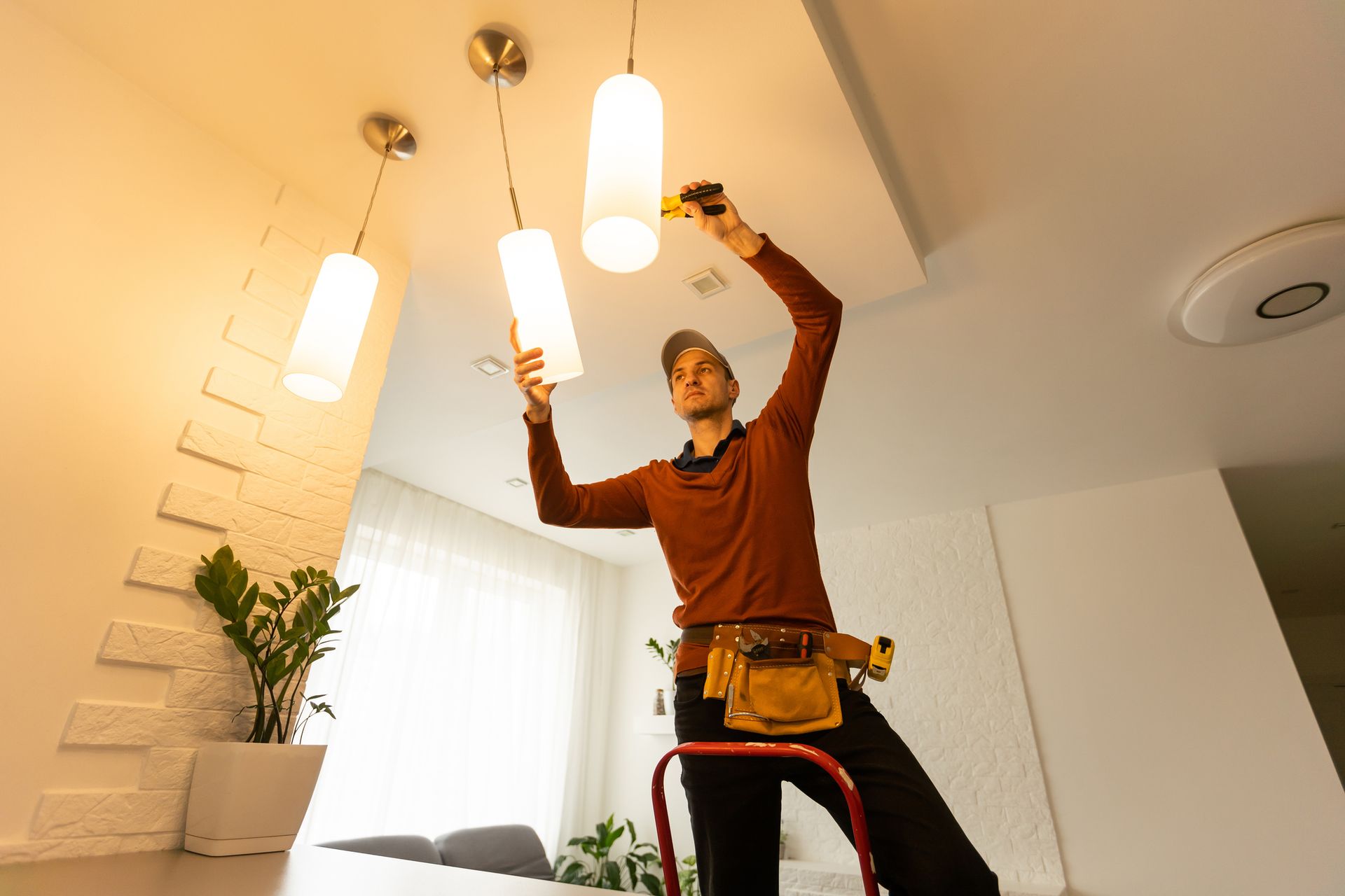 Person installing ceiling lights in a bright room with white walls and a potted plant