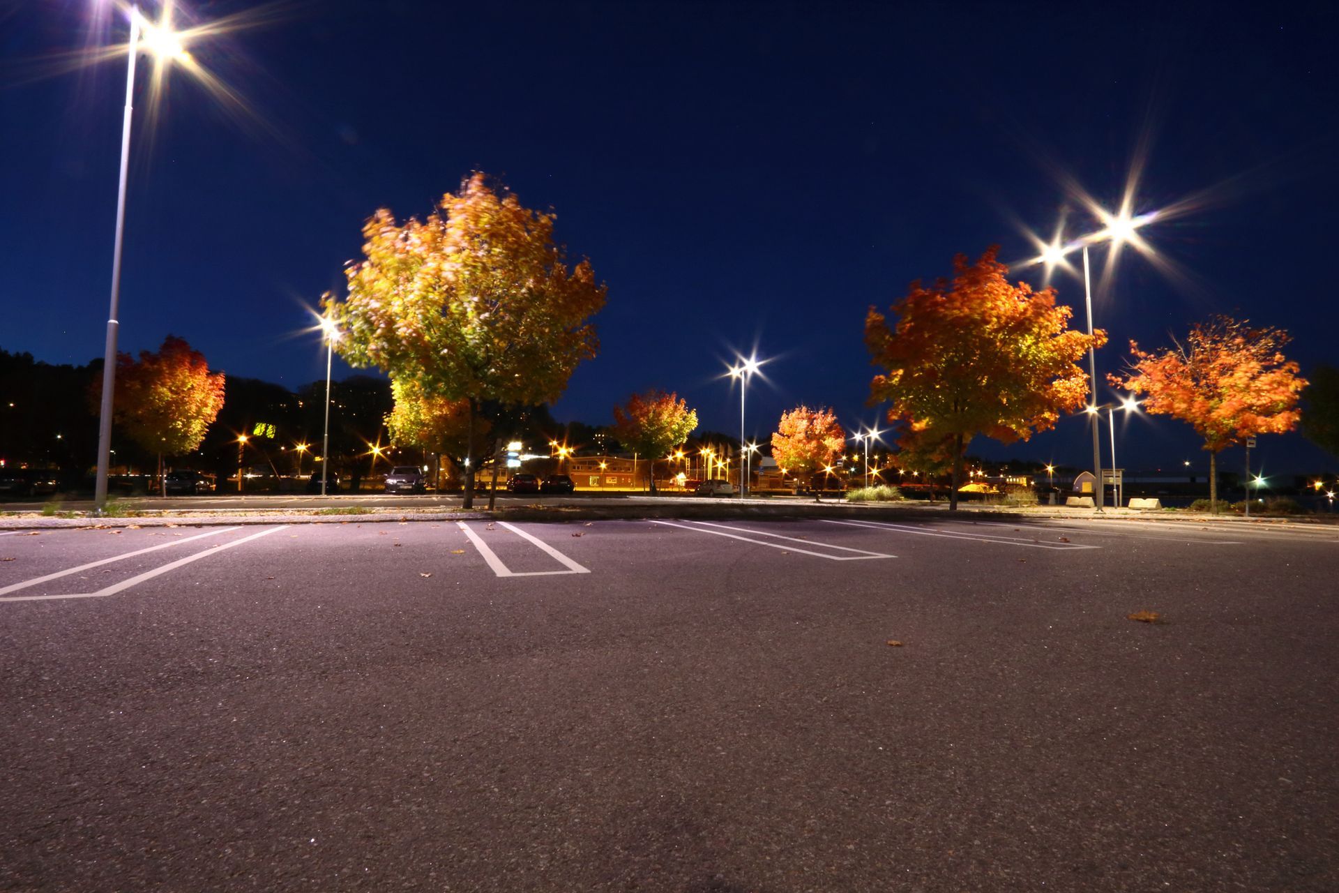 Empty parking lot at night with bright streetlights and autumn-colored trees