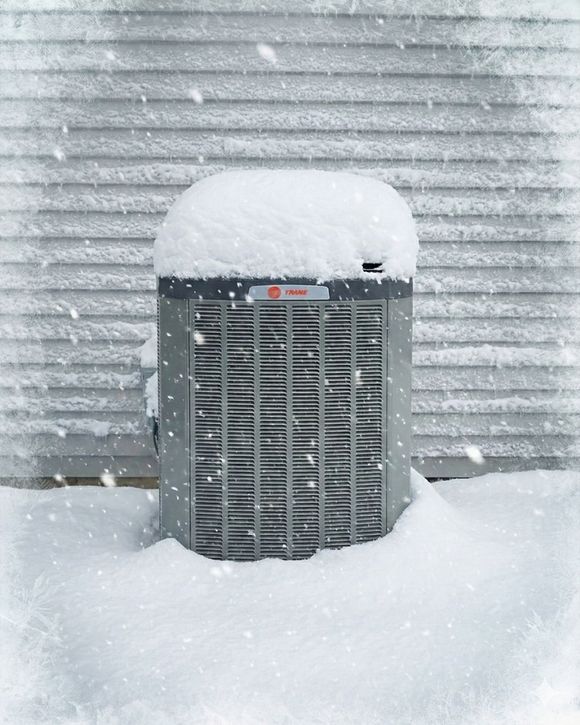 Snow-covered outdoor air conditioner against a snowy wall