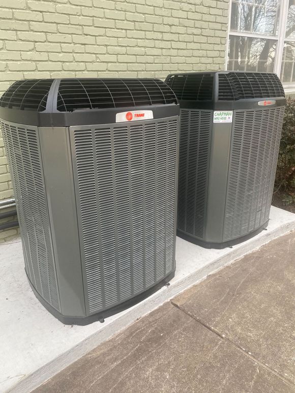Two Trane outdoor air conditioner units beside a brick wall on a concrete sidewalk
