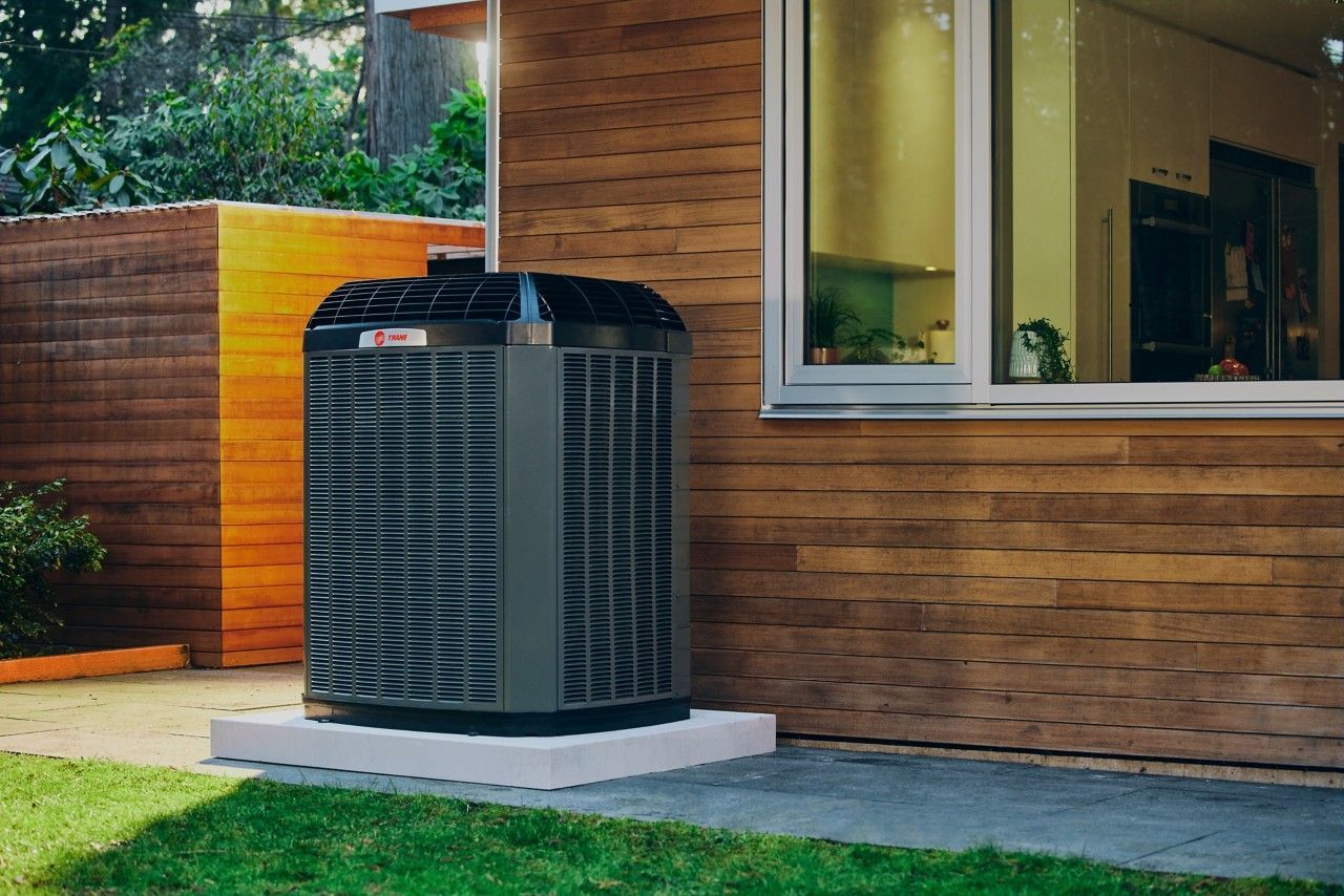 Outdoor air conditioner unit beside a wood-sided house and green lawn