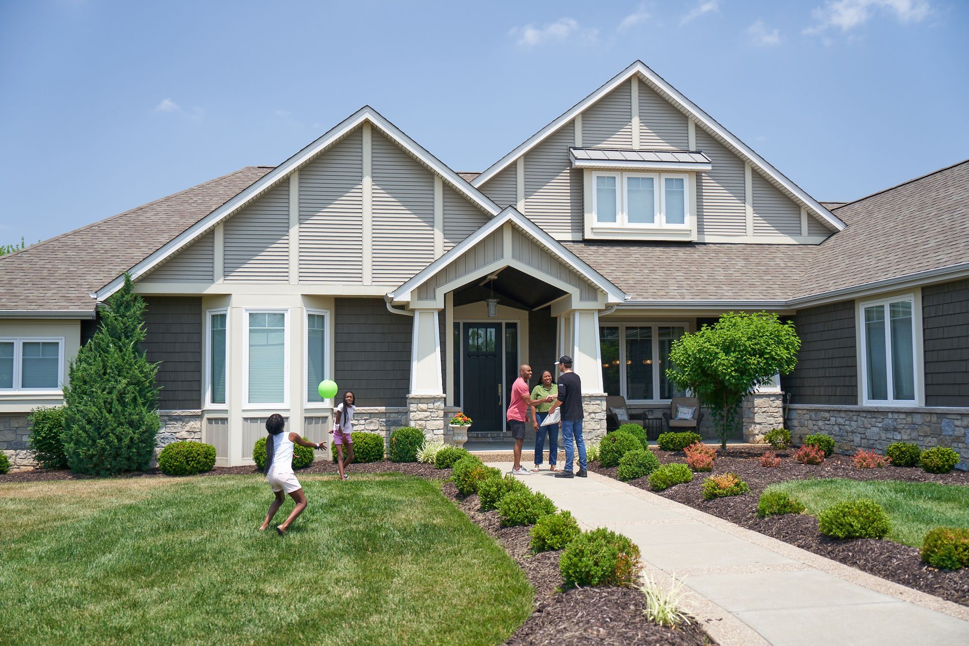 Suburban house with a manicured lawn and several people gathered on the front walkway and porch