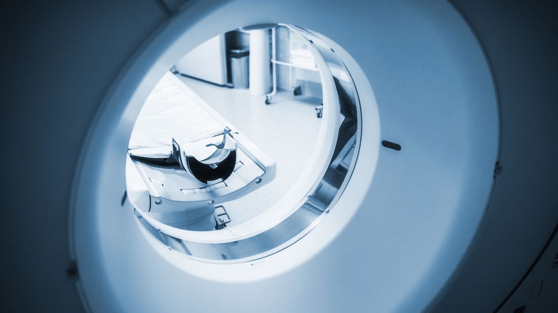 CT scanner with a person lying on the examination table inside; medical setting.