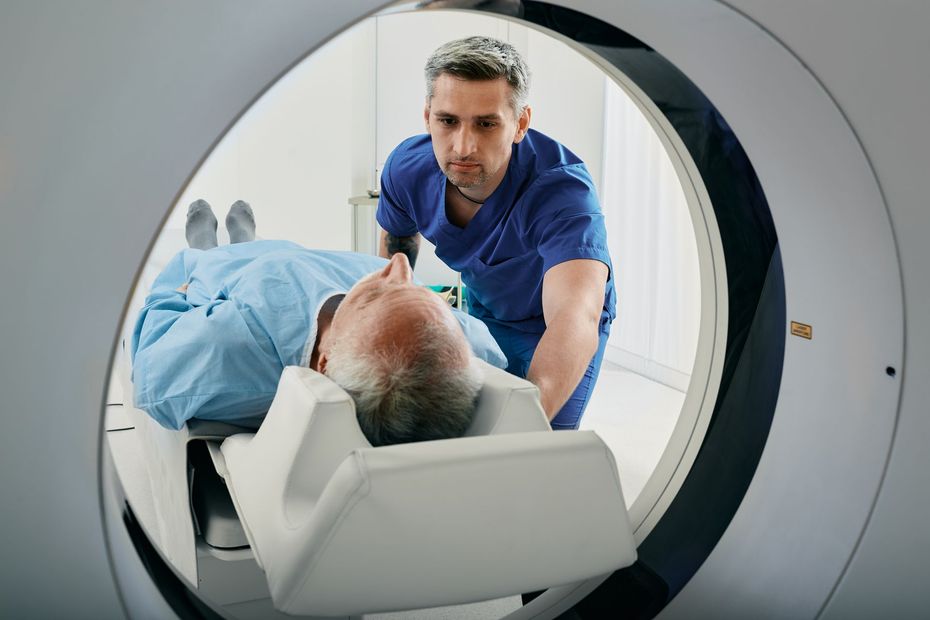 Man in a blue gown on a CT scan table, with a technician in scrubs positioning him.