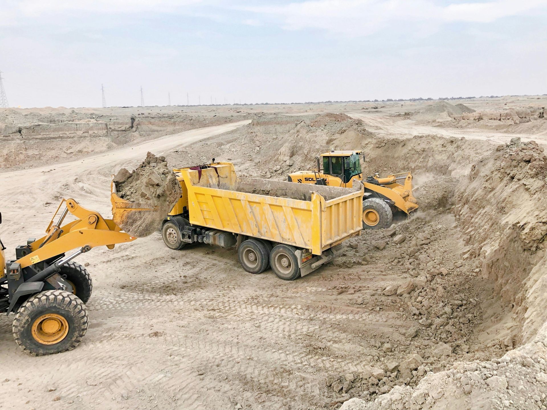 Yellow construction vehicles loading a dump truck with dirt in an open construction site.