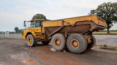 Yellow, mud-covered dump truck parked on a dirt road; a construction site setting.