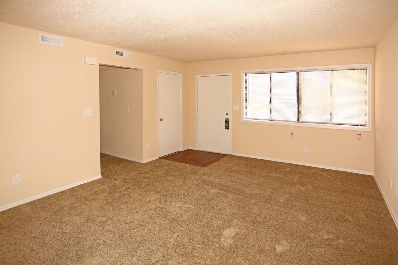 An empty living room with a carpeted floor and a window.