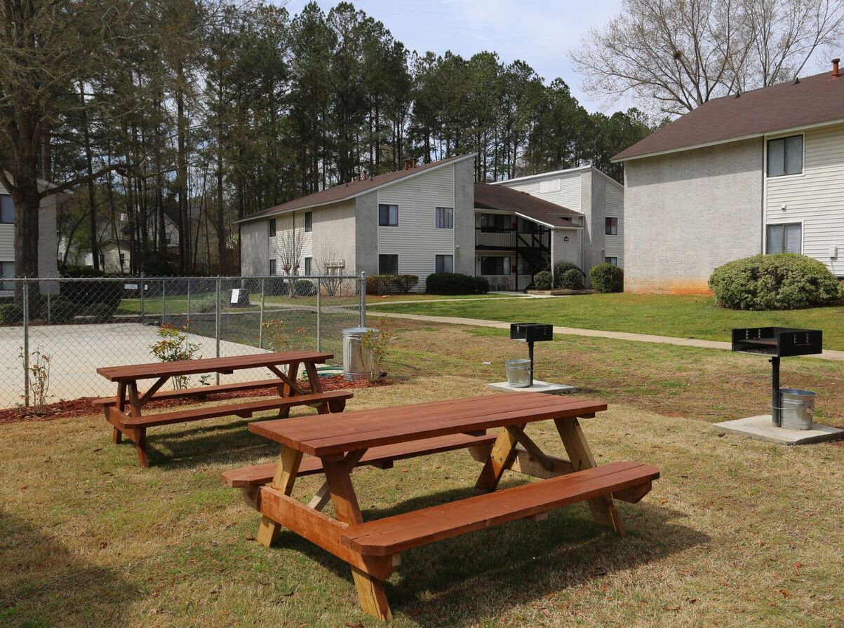 A group of picnic tables are sitting in the grass in front of a building.