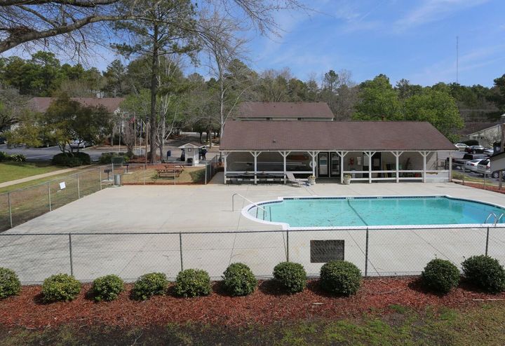 A large swimming pool is surrounded by a fence and a pavilion.