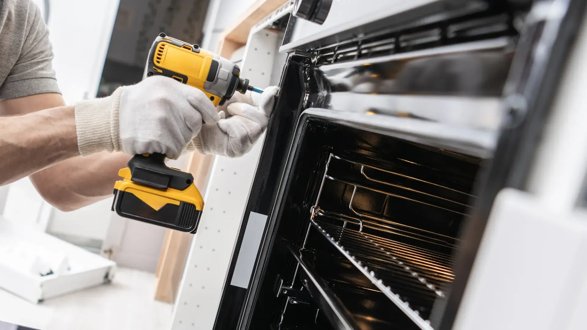 Person in gloves using a power drill to repair an oven.