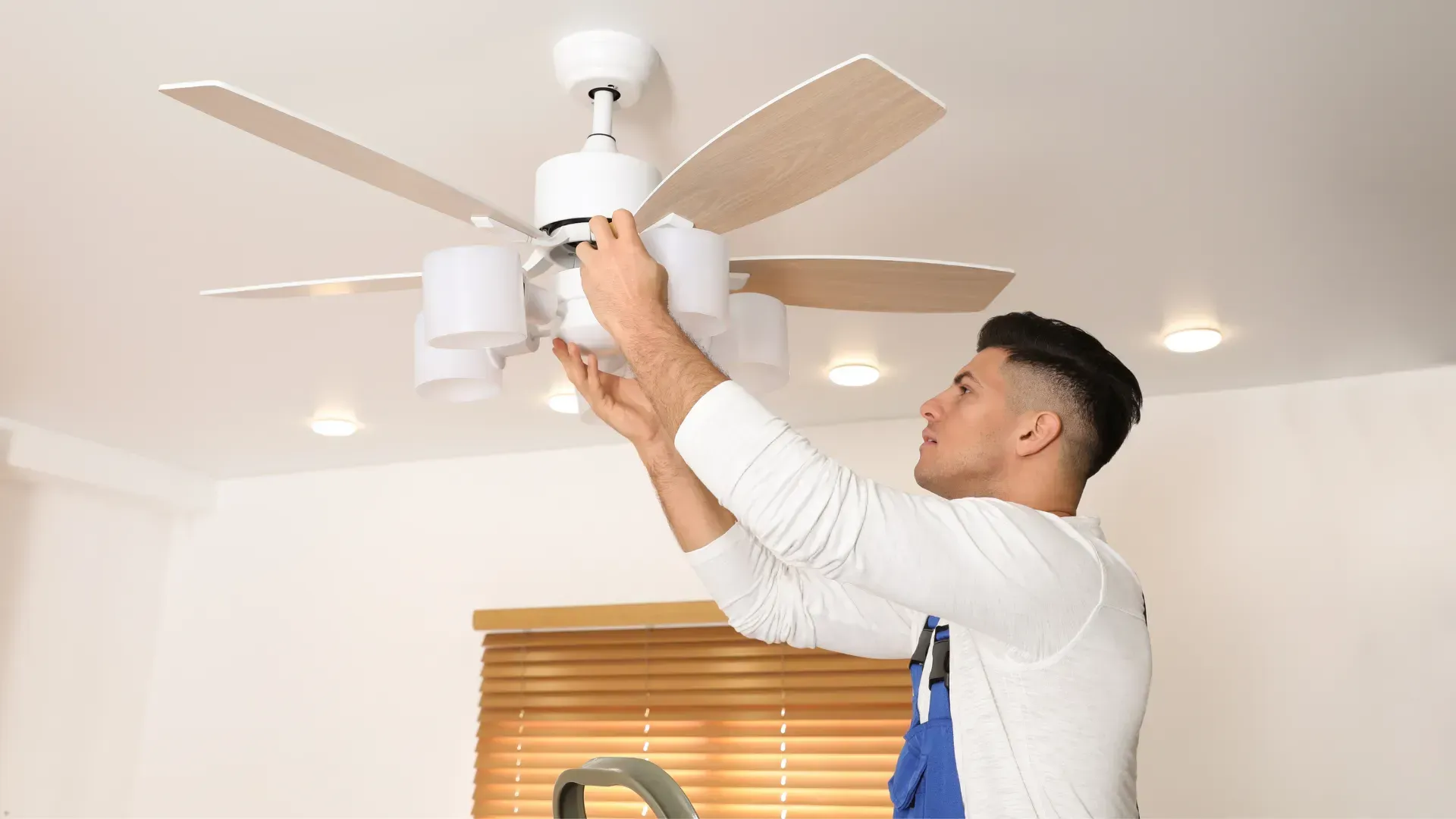 Man installing light fixtures on a ceiling fan in a room.