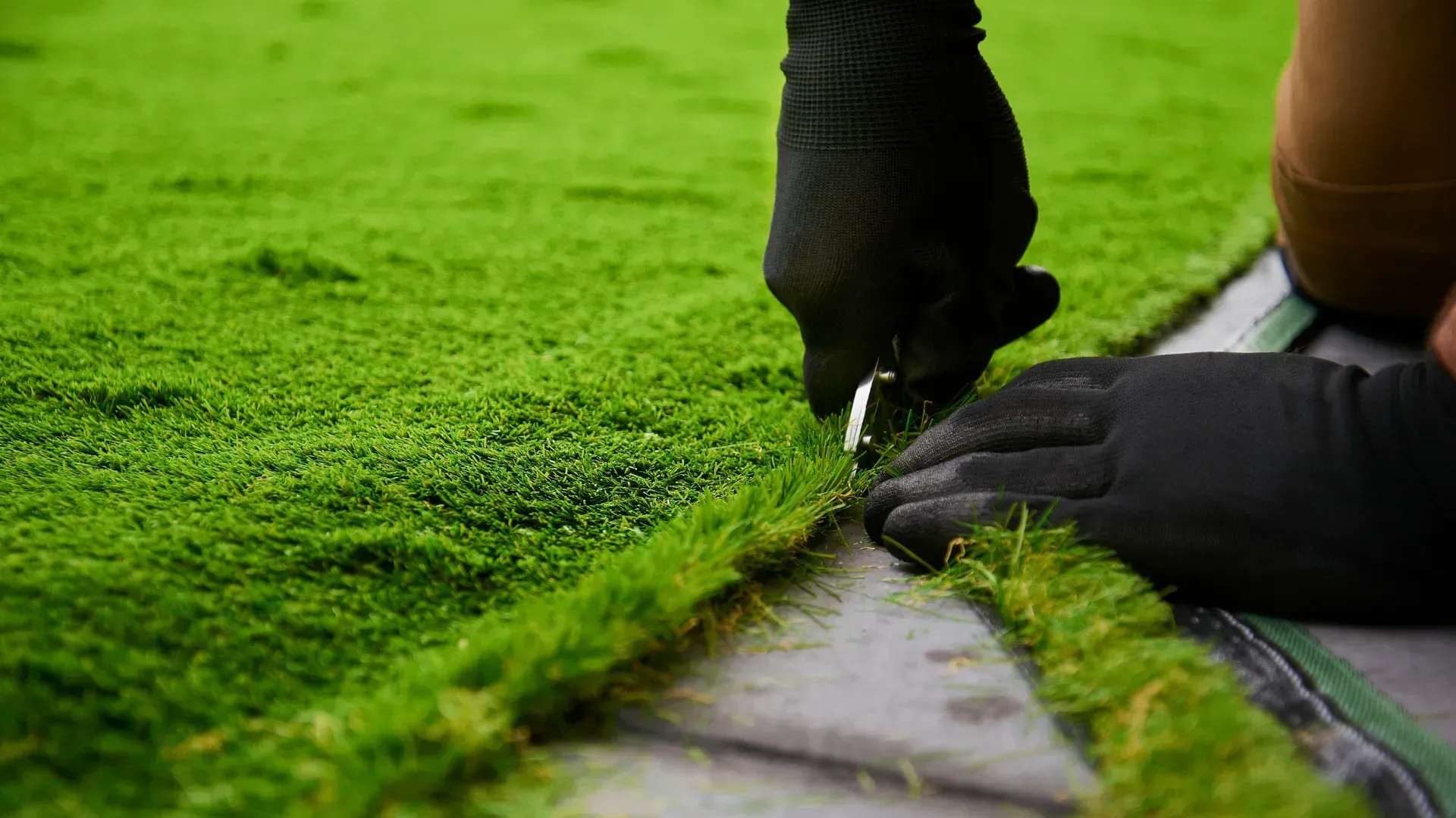 Person with black gloves cutting green artificial turf with scissors.