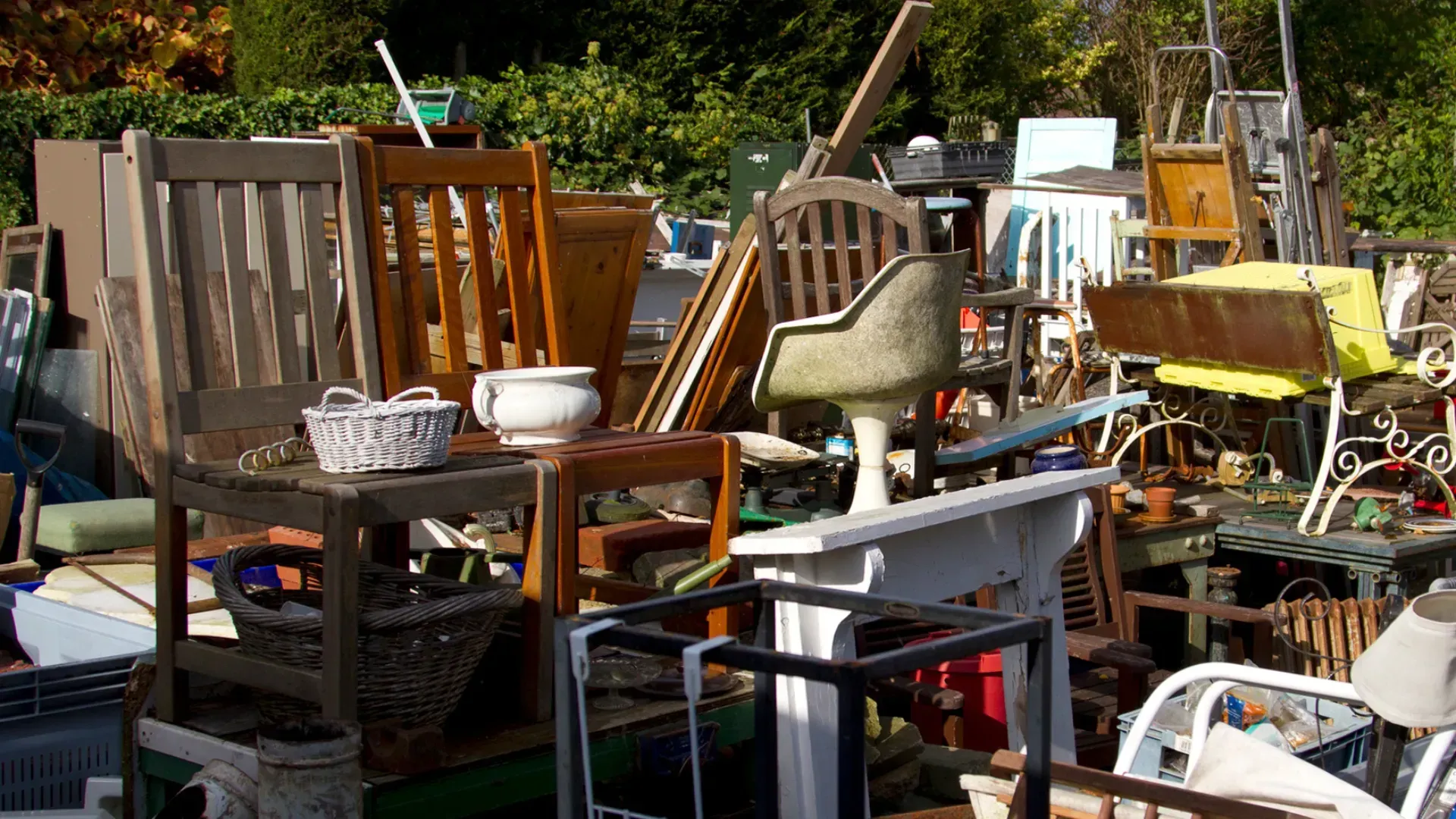 Pile of assorted used furniture for sale outdoors, including chairs, tables, and other items.