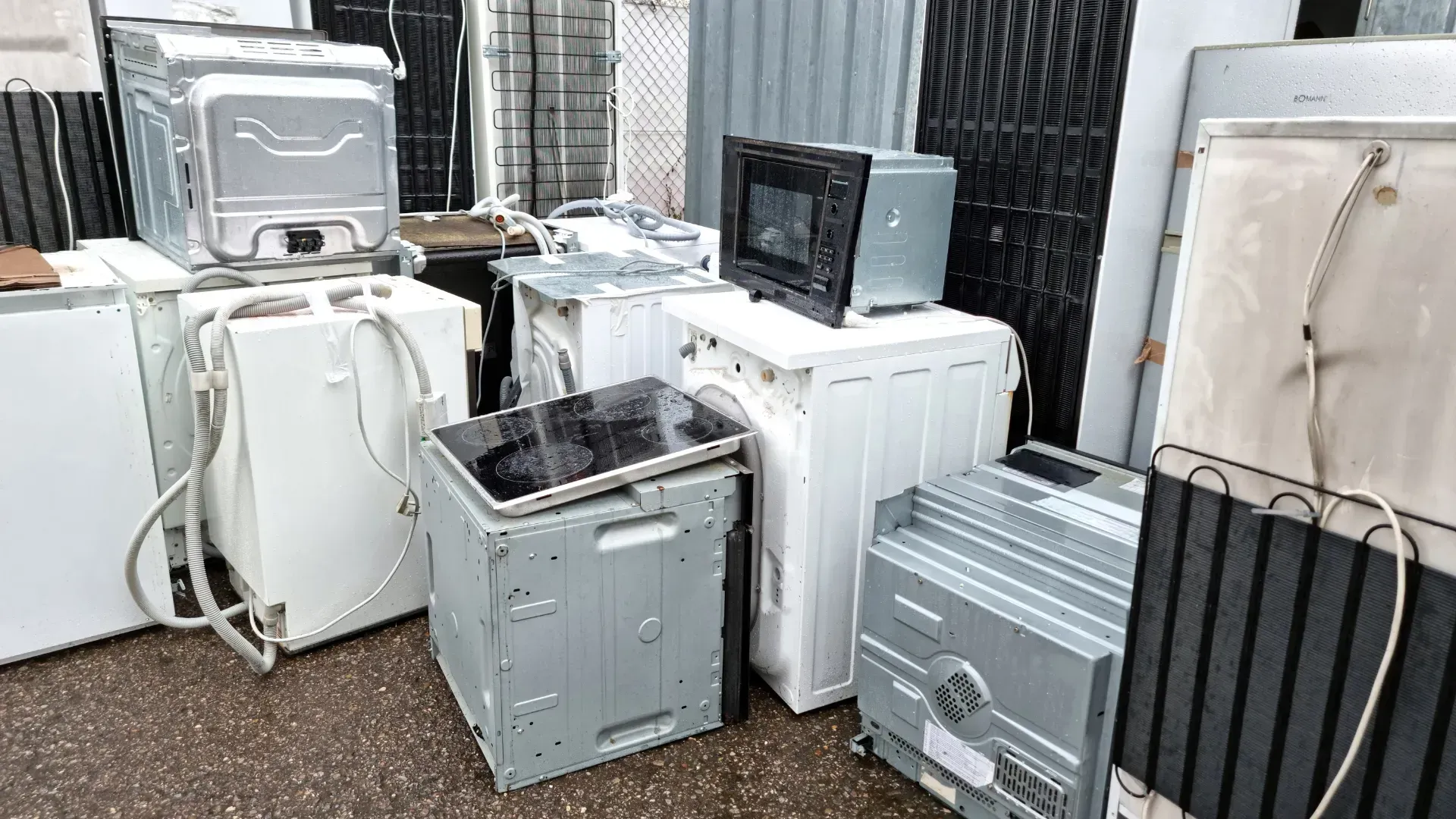 Pile of discarded appliances, including washing machines, dishwasher, microwave, and stove top.
