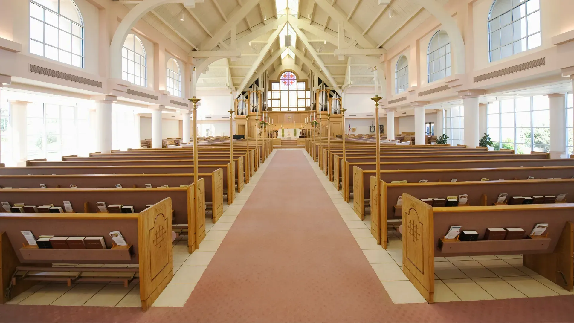 Empty church interior with rows of pews, red carpet, and light streaming through windows.