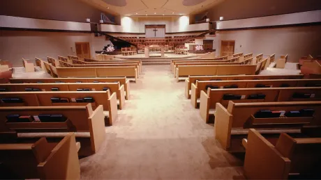 Interior view of a church sanctuary, rows of wooden pews facing the stage with a piano.