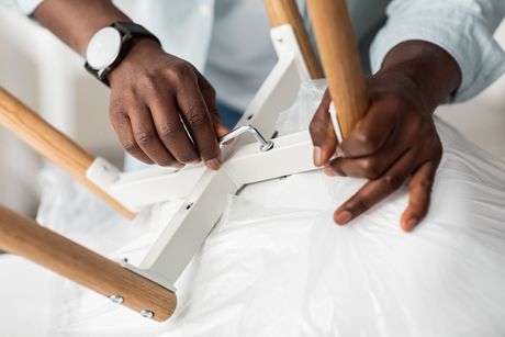 Person assembling a white chair with wooden legs, tightening a bolt.