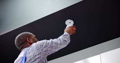 Man changing a lightbulb in a black ceiling panel; wearing a plaid shirt and overalls.