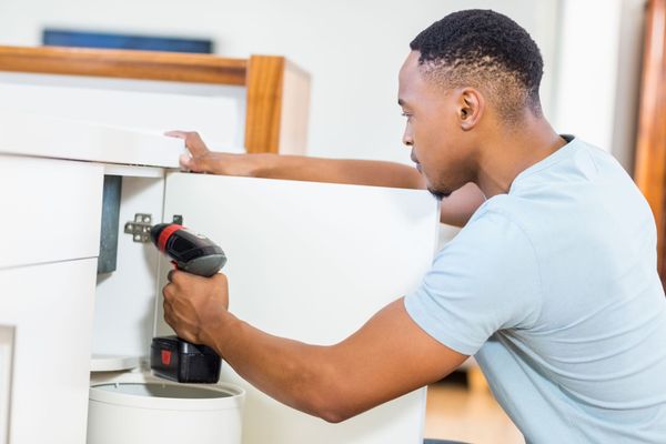Man uses a power drill to attach a cabinet door hinge indoors.