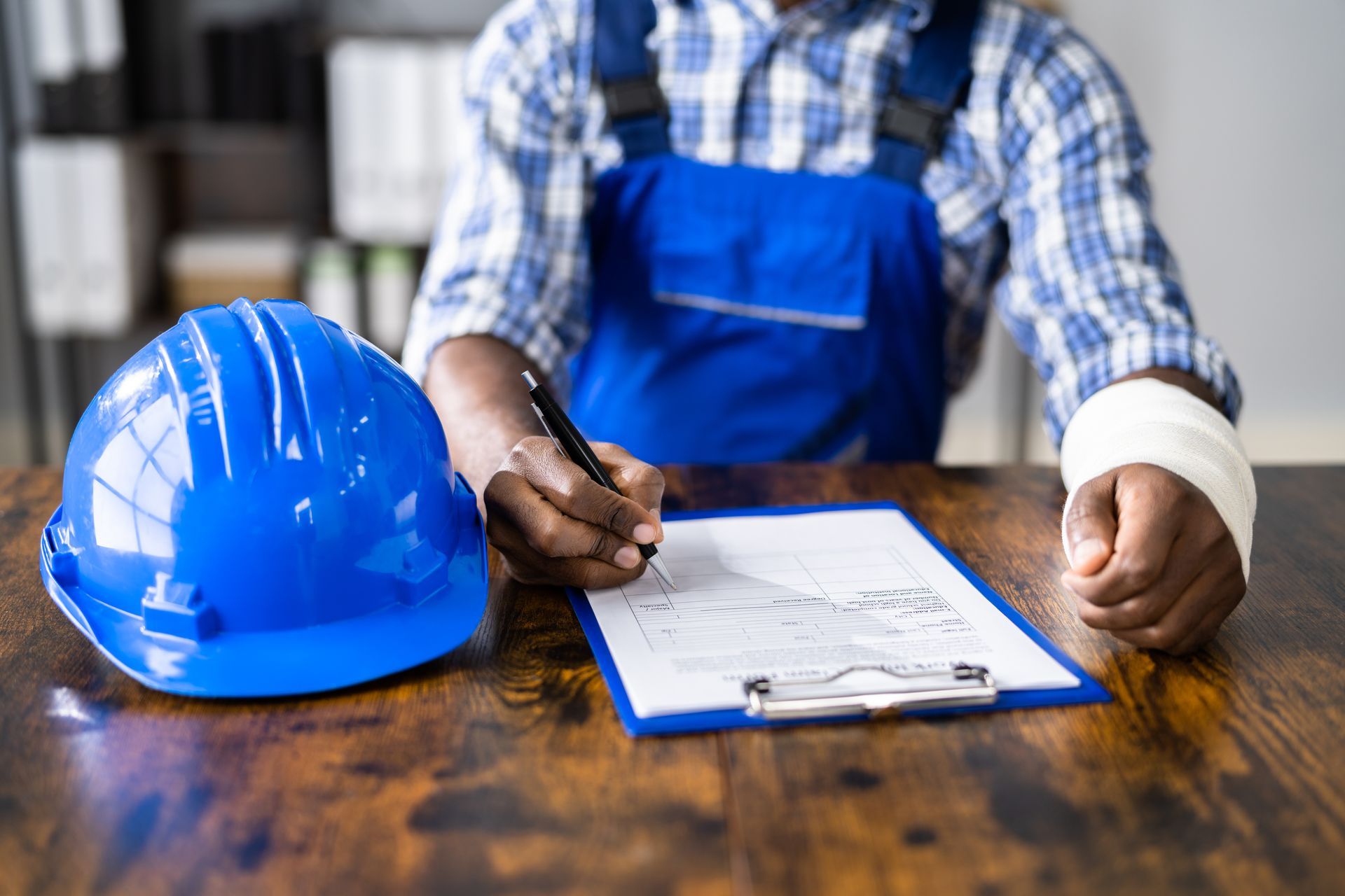 Construction worker with injured wrist filling out a form; blue hard hat on table.