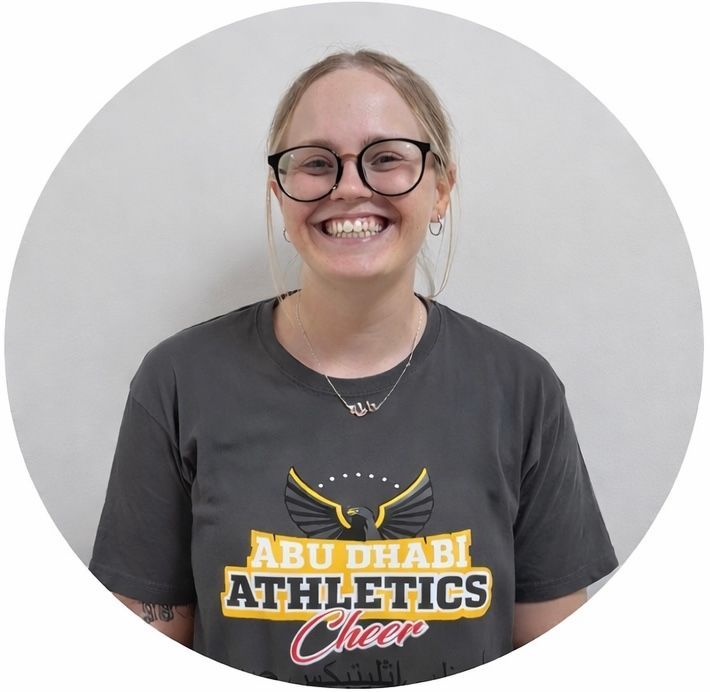 Woman wearing glasses and a gray Abu Dhabi Athletics Cheer t-shirt, smiling.